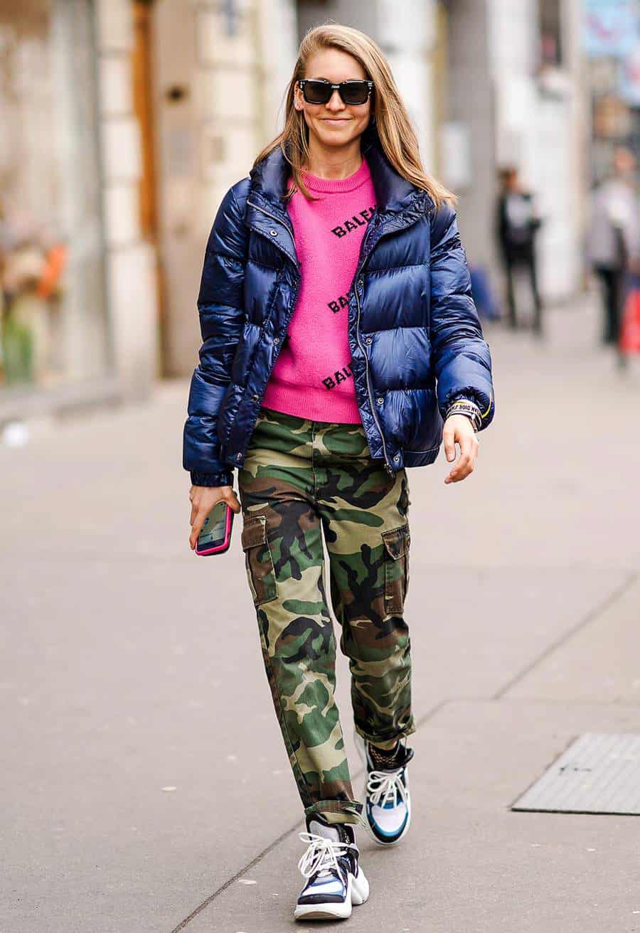 A woman wearing camo pants with a bright pink shirt and a dark purple puffer jacket