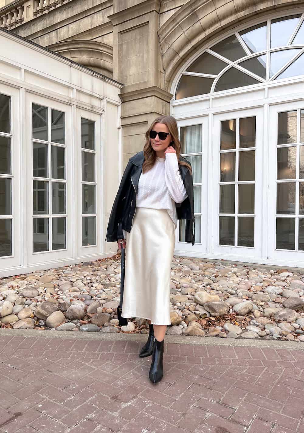 Christal wearing a satin midi skirt with a white sweater and a black leather jacket.