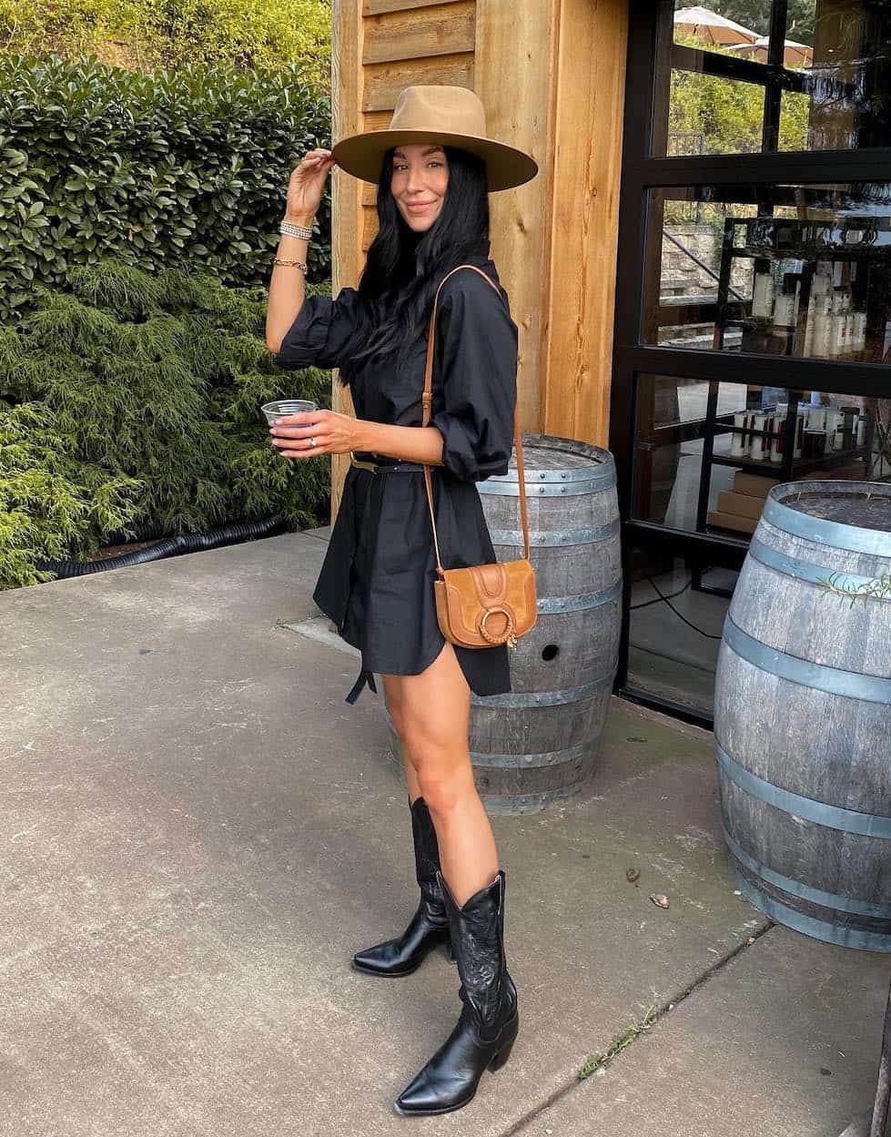 woman at a winery wearing a tan fedora, black dress, and black cowboy boots
