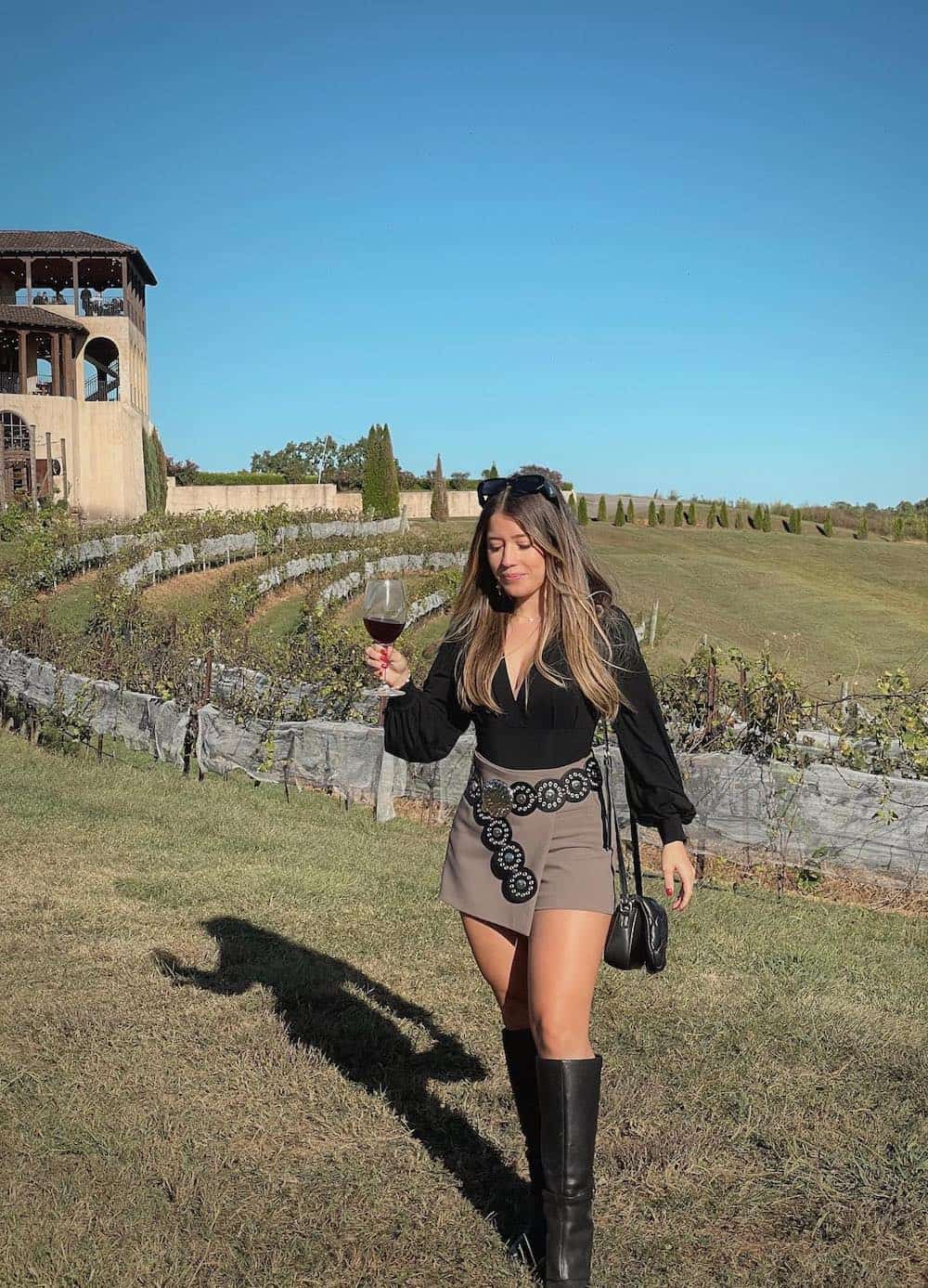 a woman wearing a taupe mini skirt, a black bell sleeve top, and tall black boots
