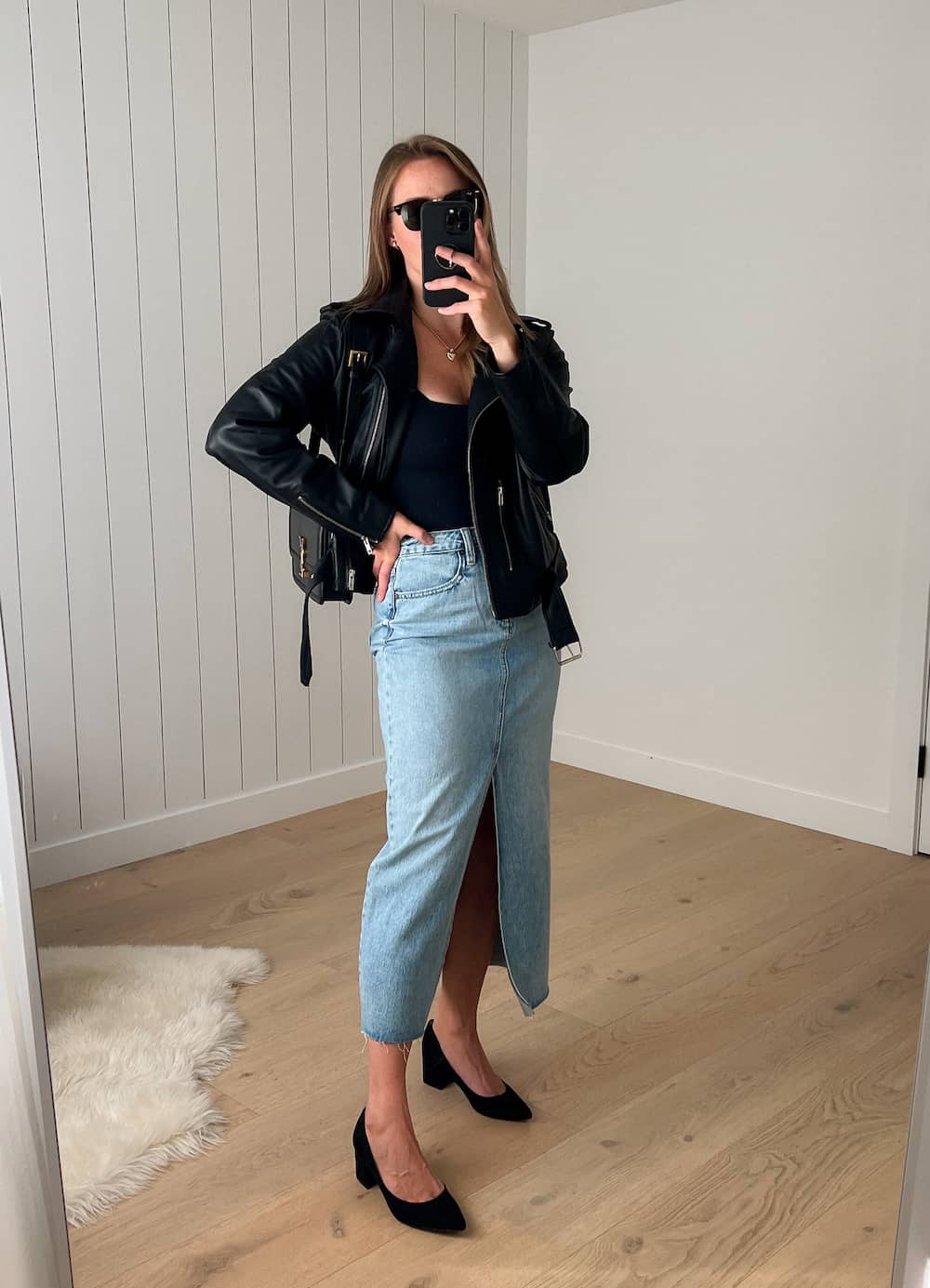 woman wearing a winter concert outfit with a leather jacket, denim midi skirt and black suede heels