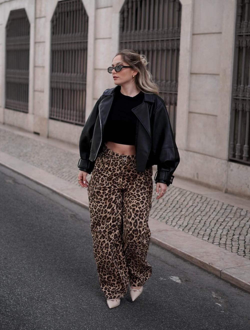 a winter concert outfit featuring cheetah print pants, a black crop top, a black leather jacket, and classic pumps