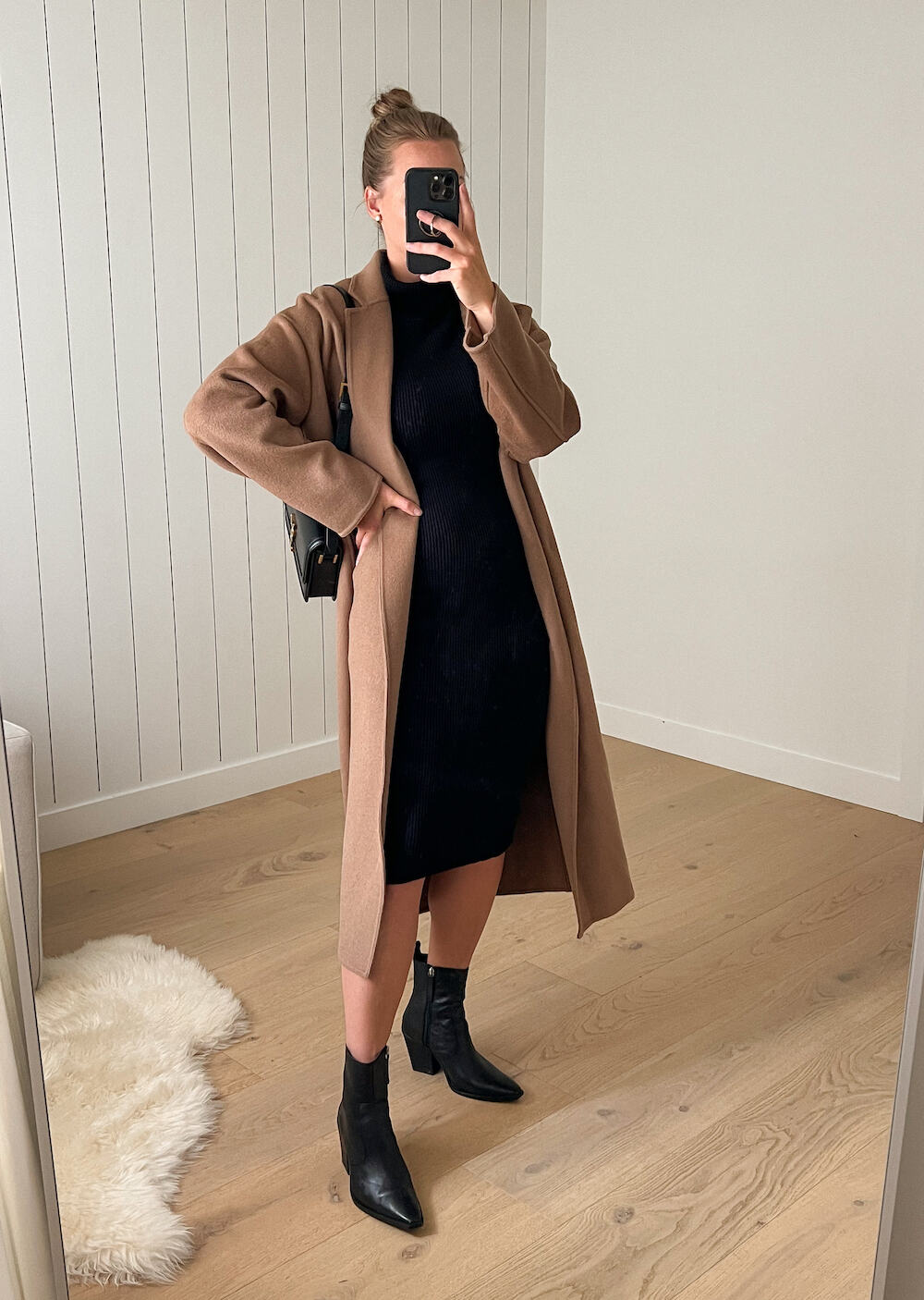 Woman wearing a black sweater dress with ankle black boots and a long brown coat for a winter concert