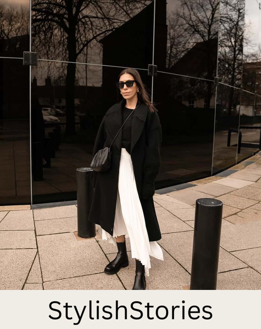 woman wearing a black long coat with a pleated ivory skirt and black boots