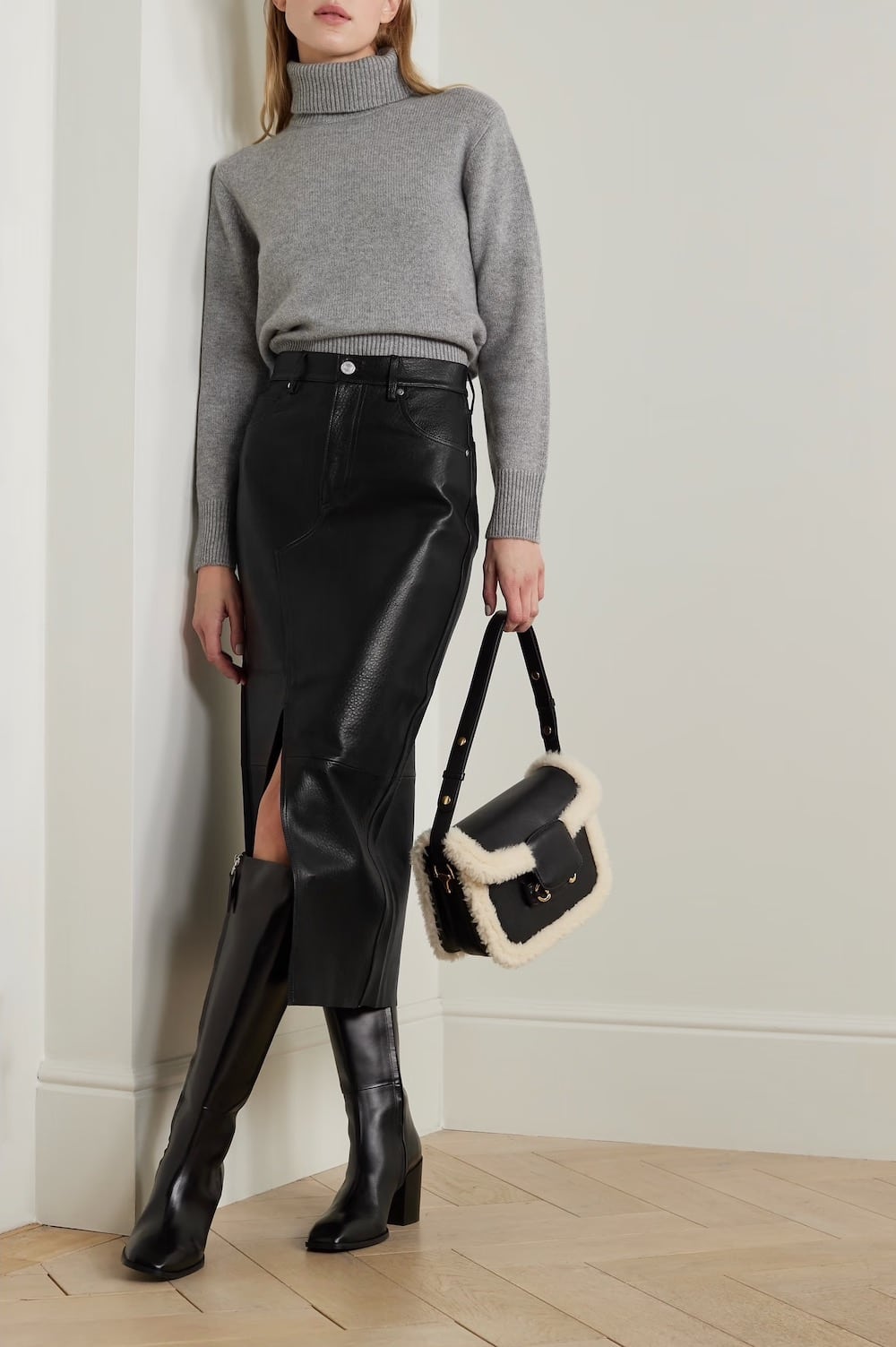 Woman wearing a black long denim skirt with tall black boots and a grey turtleneck.
