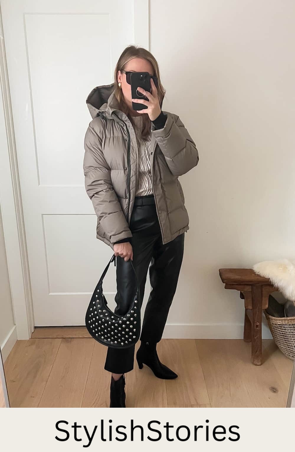 Christal wearing leather pants, black booties and a grey puffer coat with a studded black bag.