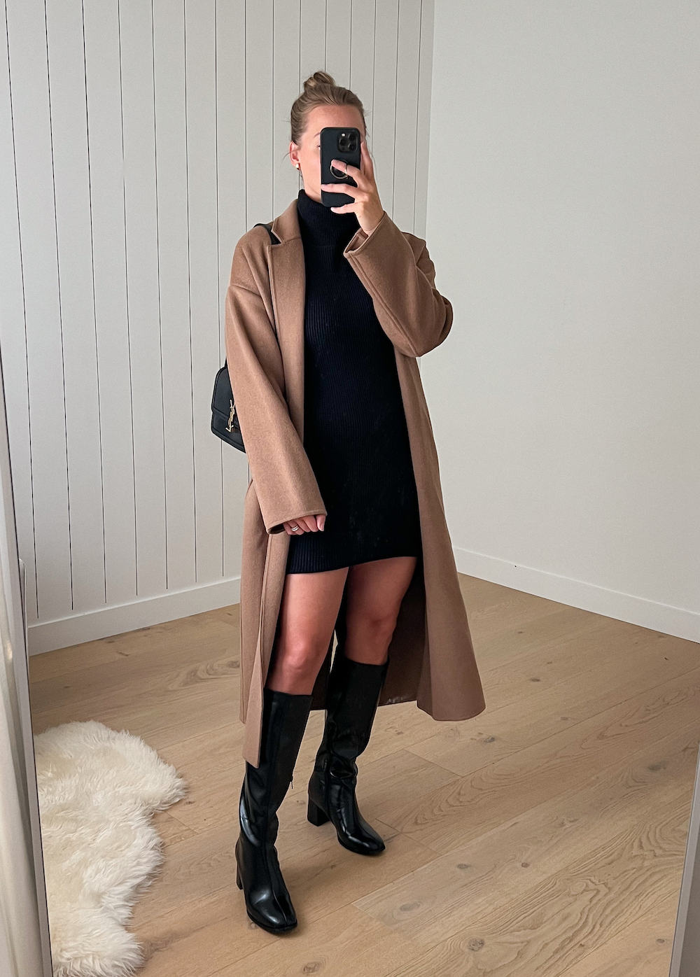 Christal wearing a black sweater dress and tall black boots with a camel colored coat.