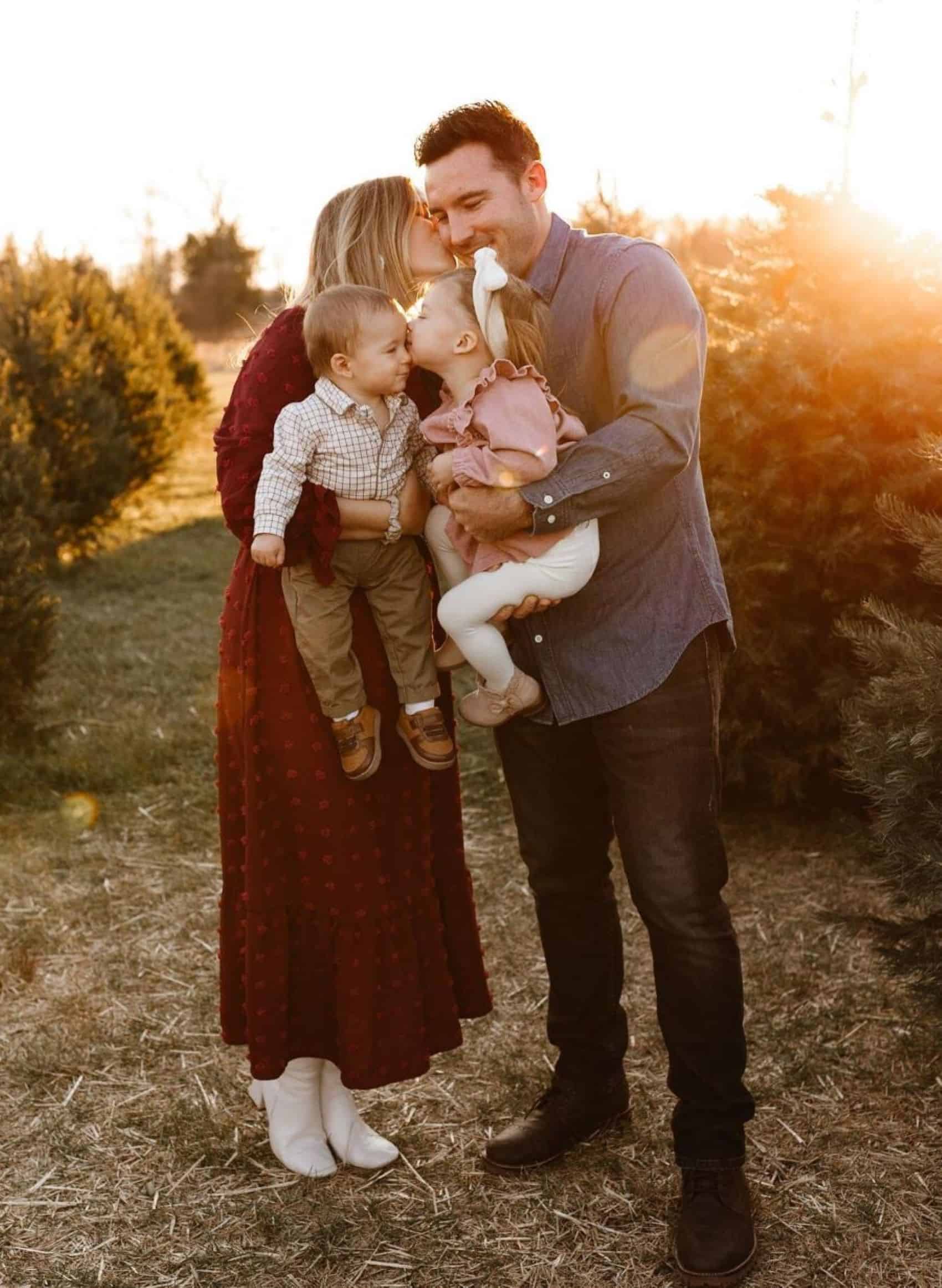 A winter family photo where the mother is wearing a long-sleeved red dress, and the father and son are wearing button-up shirts, while the daughter wears a ruffled dress