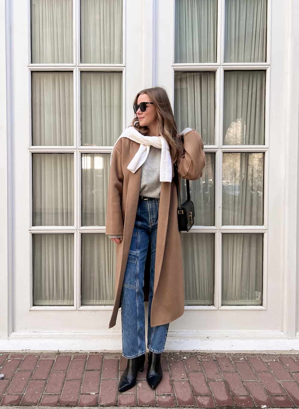 Christal wearing jeans with black booties a grey sweater and a brown coat.