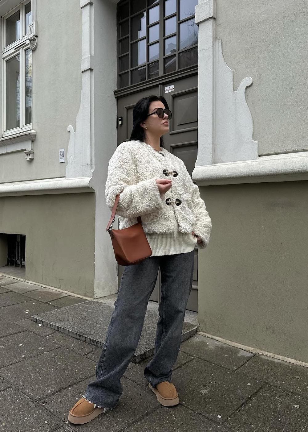 Woman wearing baggy jeans and a textured coat with Ugg boots.