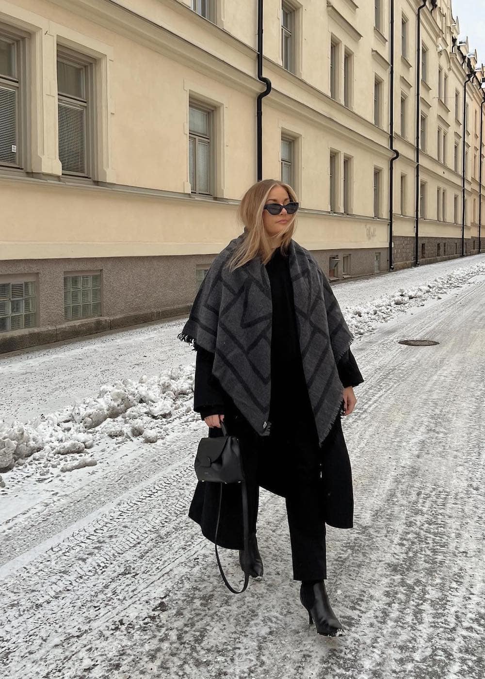 Woman wearing a black trench coat with black pants and black booties with a gray and black geometric print scarf.