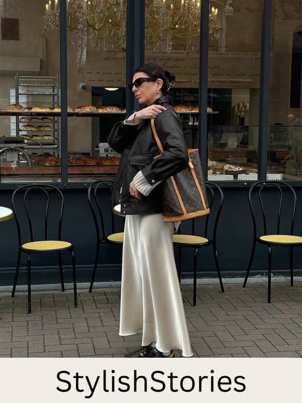 Woman wearing a white satin slip skirt with a black coat and sambas.