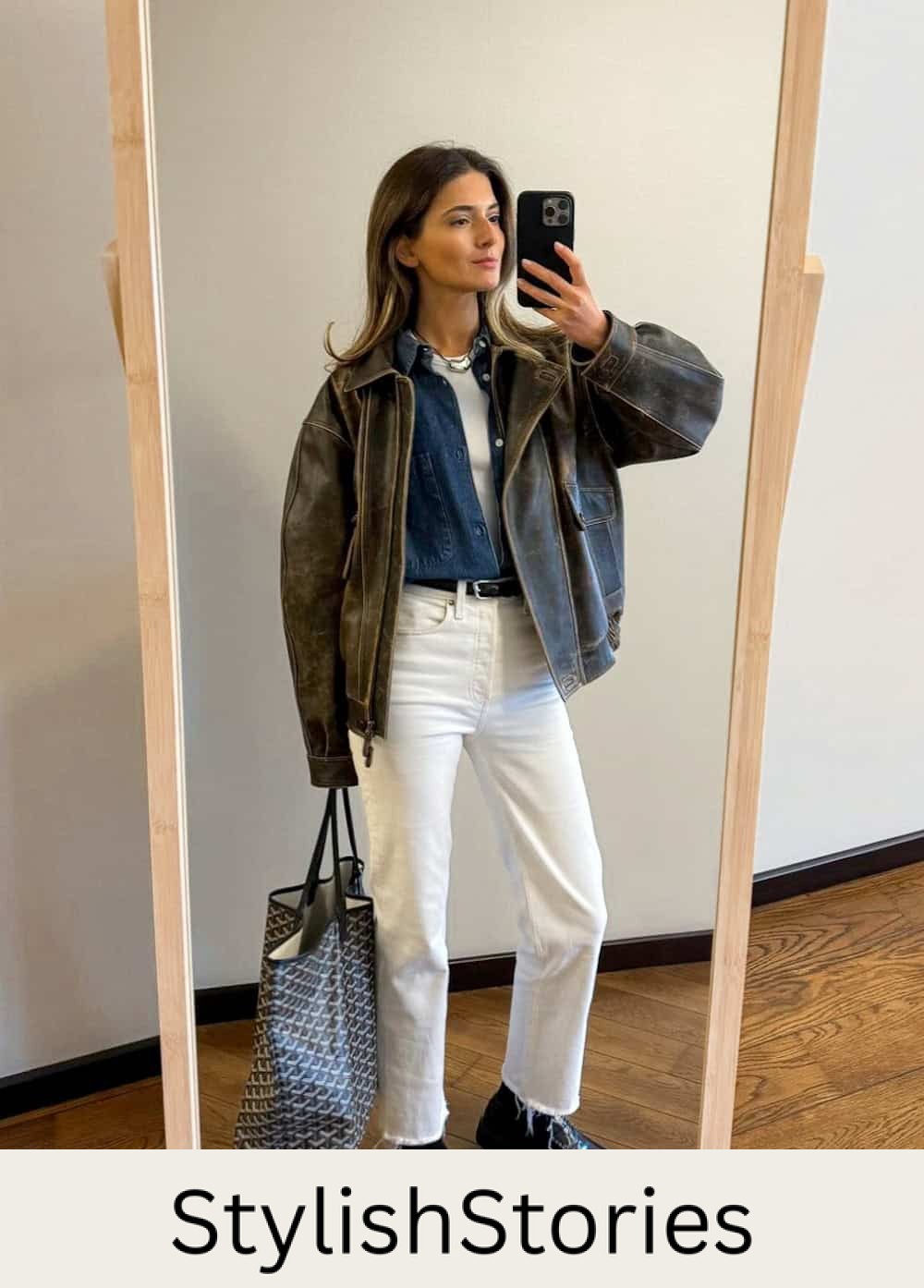 Woman wearing white jeans with black loafers and a leather jacket.