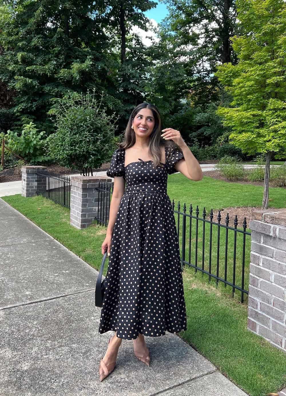 Woman wearing a black and white polka dot dress with nude pumps.