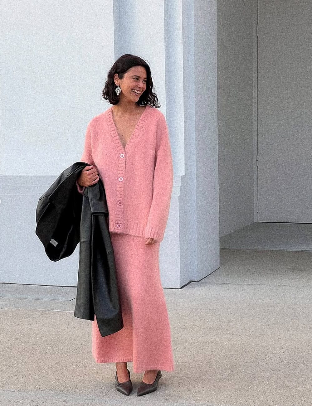 Woman wearing a pink sweater and skirt set with pumps.