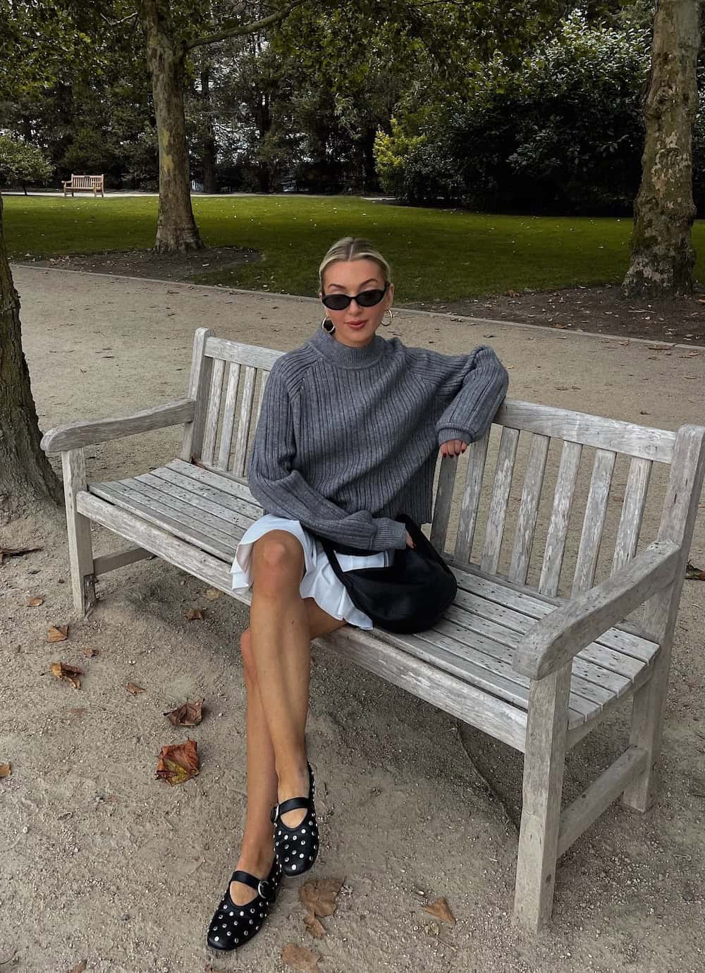 Woman wearing a white skirt with a grey sweater and ballet flats.