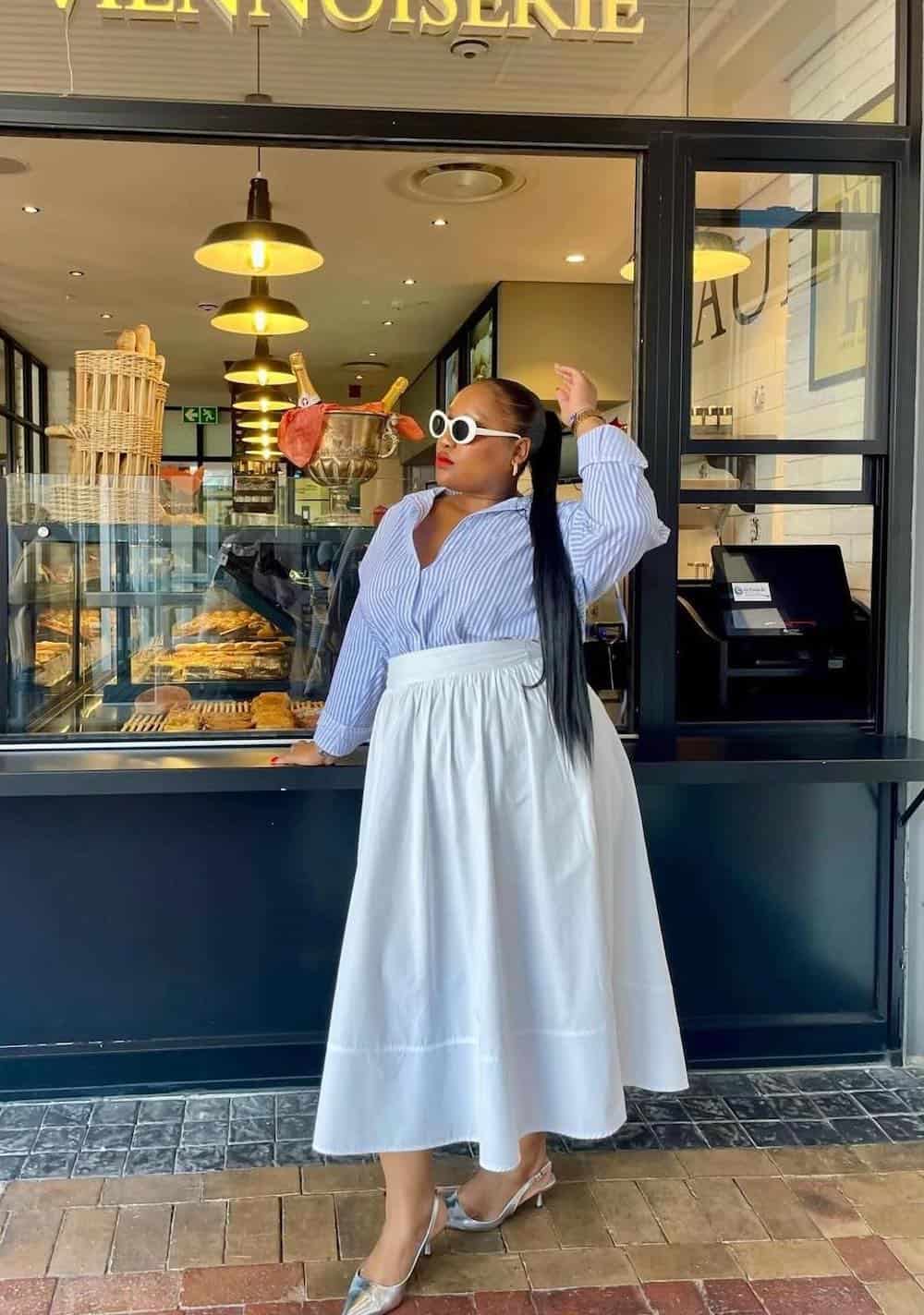 Woman wearing a white poplin skirt with a blue and white striped button down and silver heels.