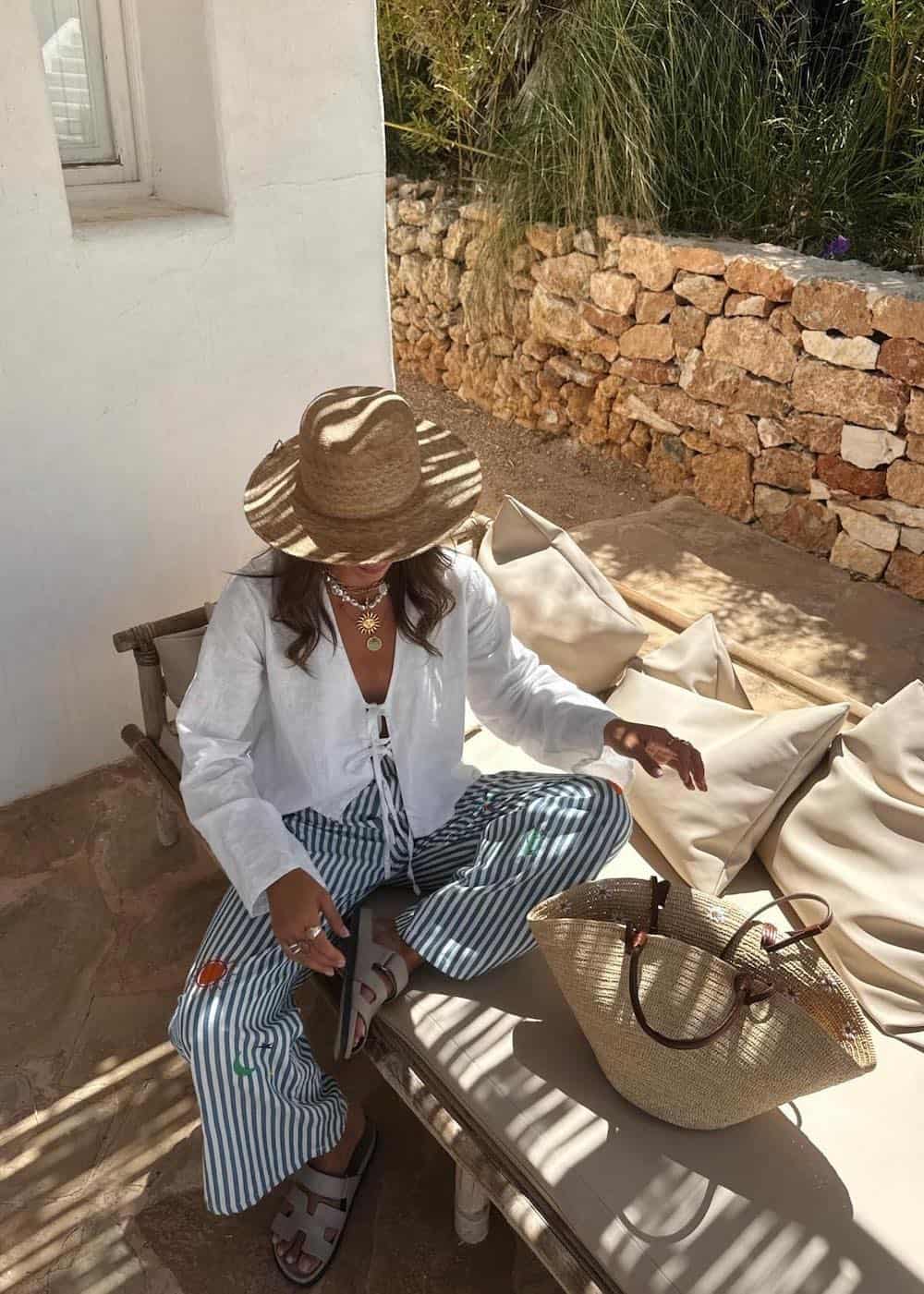 Woman wearing white and blue striped pants with a white linen top and a straw hat.