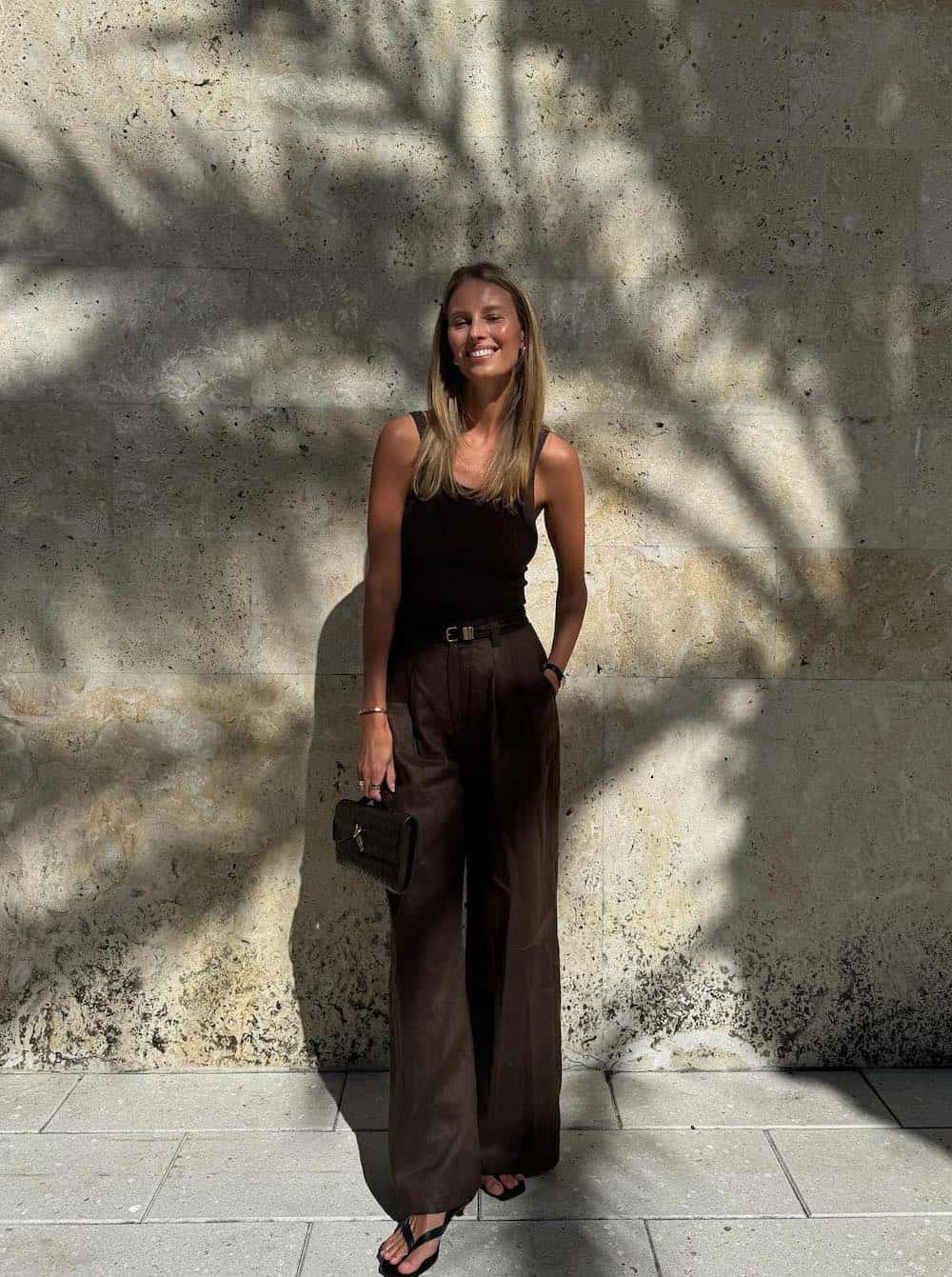 Woman wearing brown trousers with a brown tank top and heeled sandals.