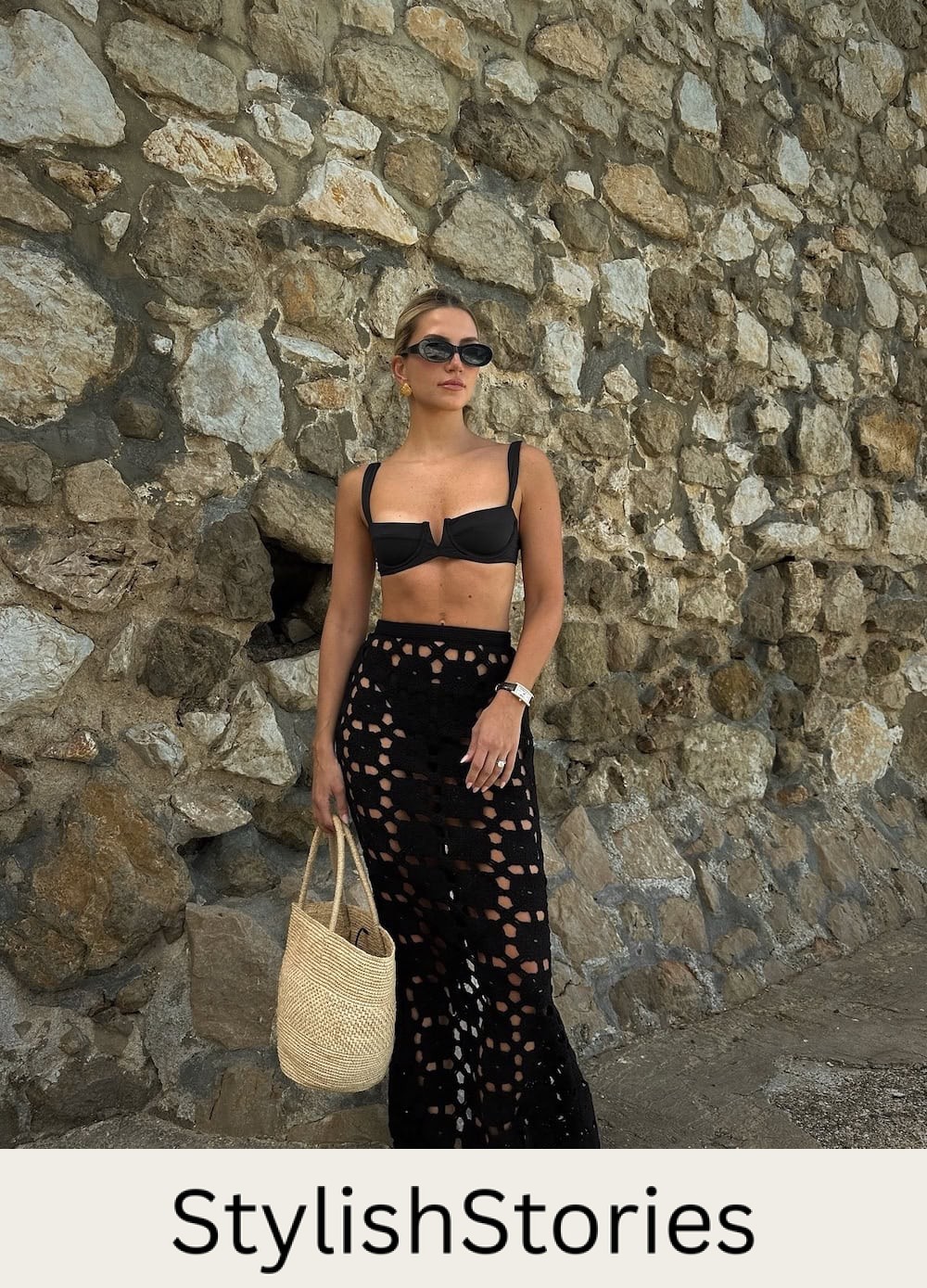 a woman wearing a black bikini with a see through crochet black skirt and a raffia tote