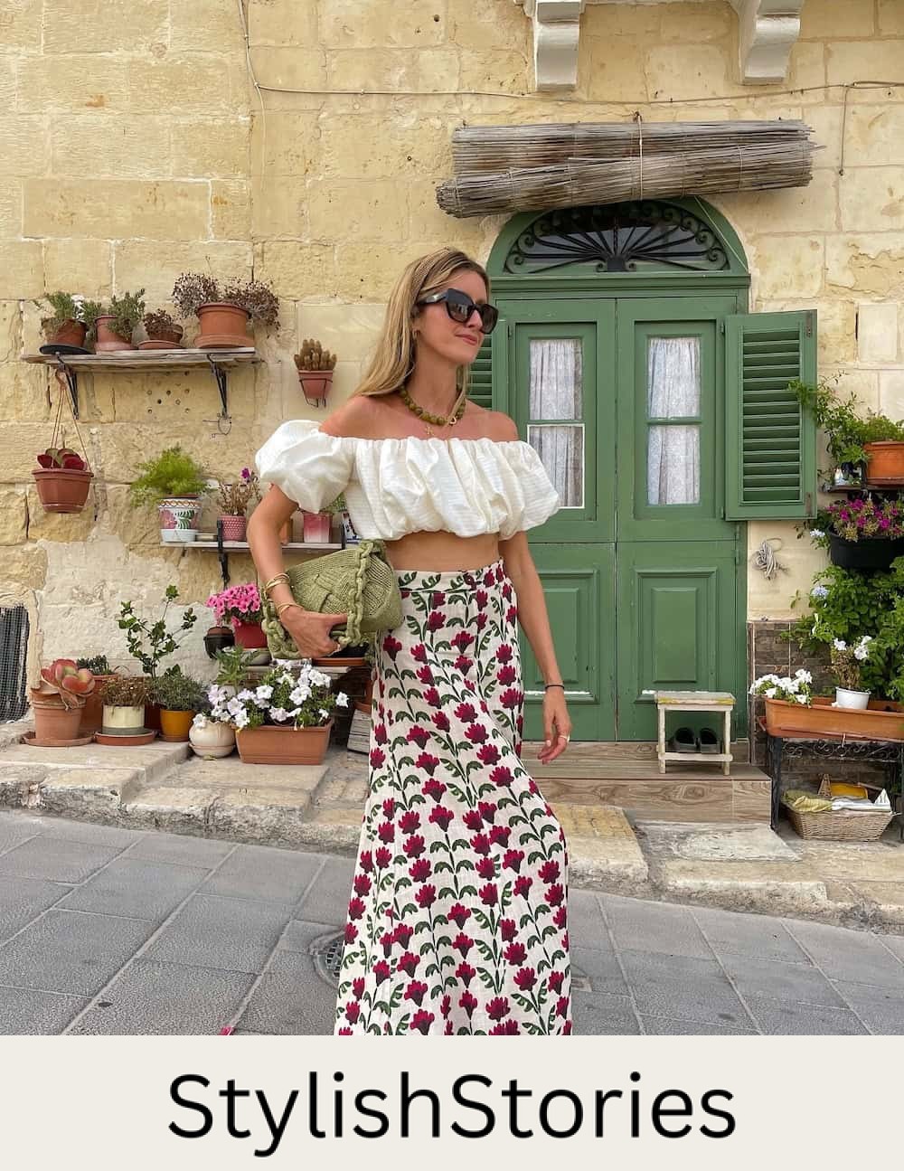 a woman wearing a floral maxi skirt and a puffed off the shoulder top with a green handbag