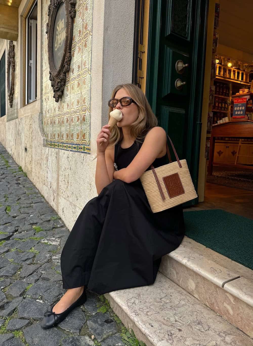 a woman wearing a black maxi dress with black ballet flats and a raffia and brown leather tote
