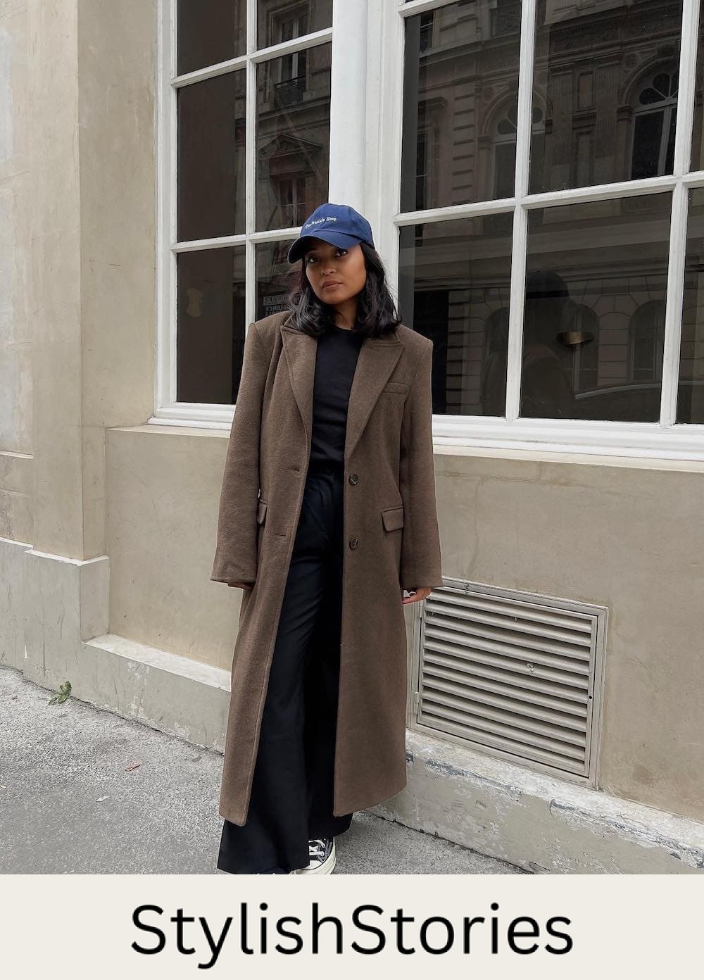 Woman wearing black wide leg pants with sneakers and a long brown coat.