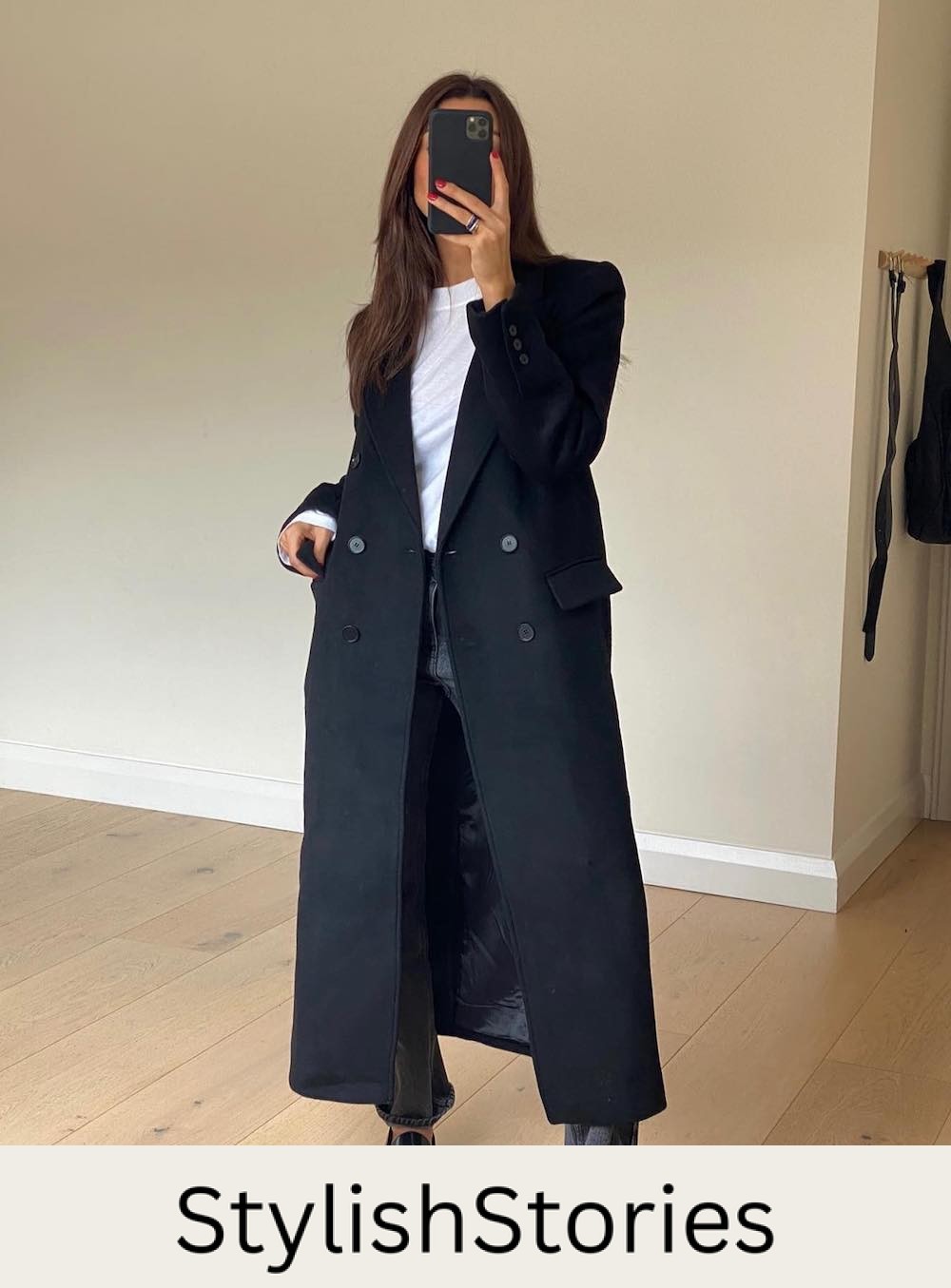 Woman wearing jeans, a white tee and a long black coat.