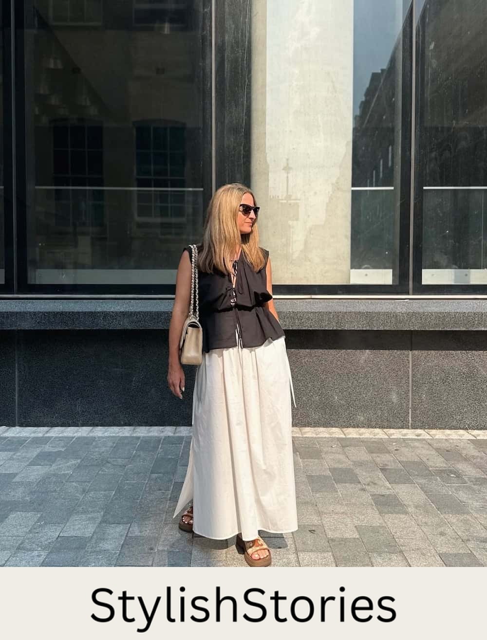 Woman wearing a white maxi skirt with a black vest top and chunky sandals.