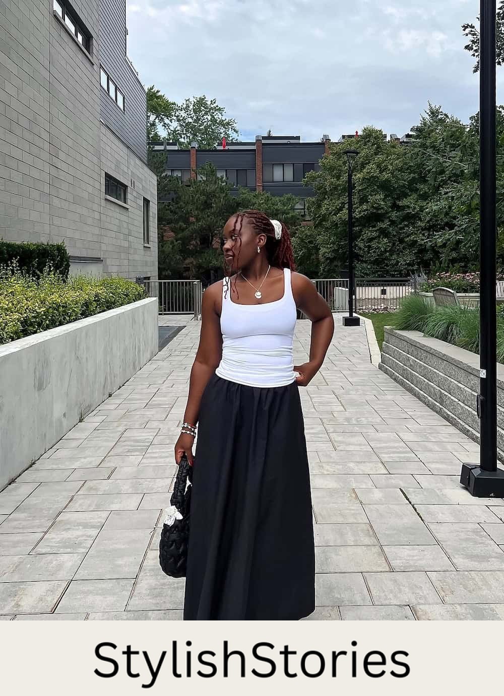 Woman wearing a black maxi skirt with a whit tank top and sneakers.