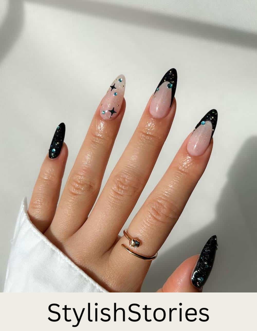 long nude almond nails with a glitter basecoat, black frecnh tips nails, and solid black nails featuring blue gem accents
