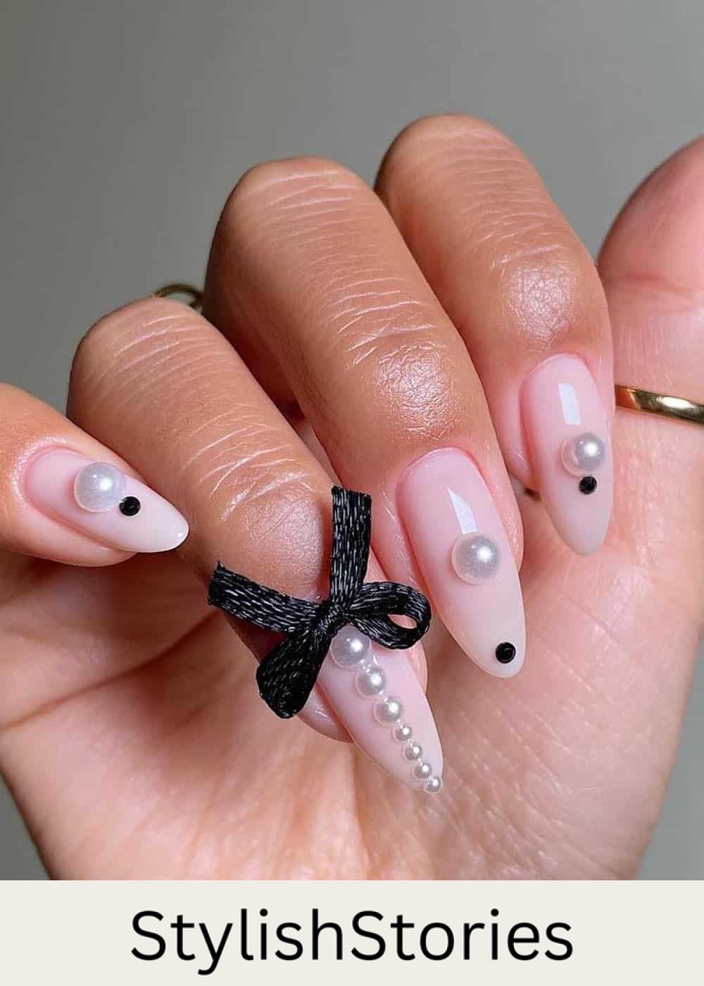 long nude pink pointy nails with pearls, black gems, and black bows