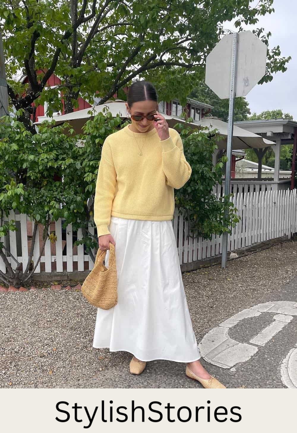 Woman wearing a white skirt with a yellow sweater and nude flats.