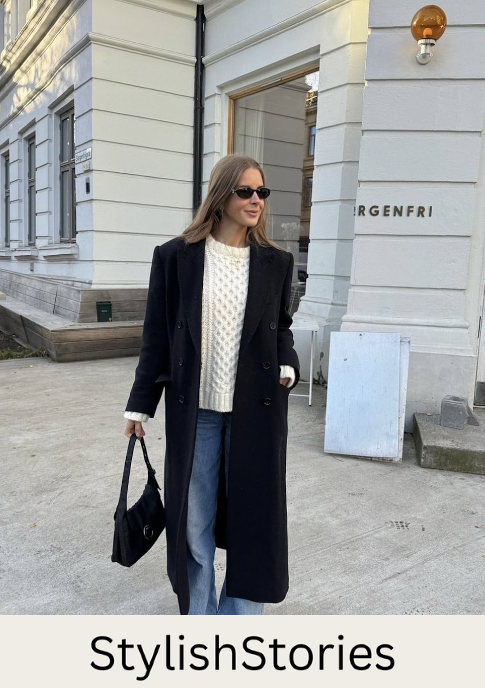 Woman wearing jeans, a white chunky knit sweater and a black coat.