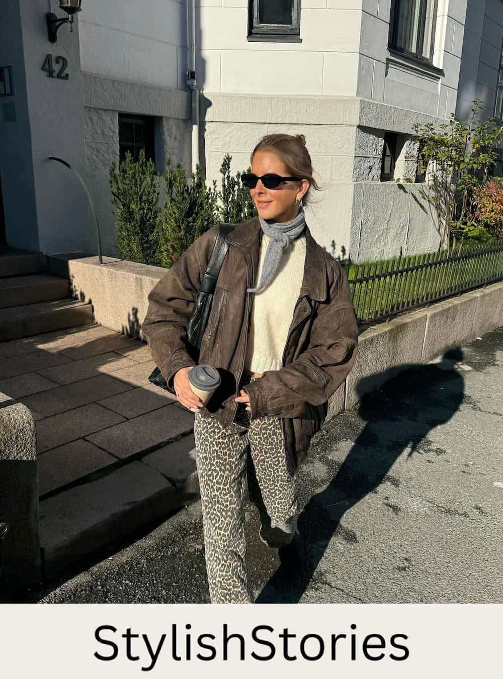 Woman wearing animal print pants with a white sweater and an aviator jacket.