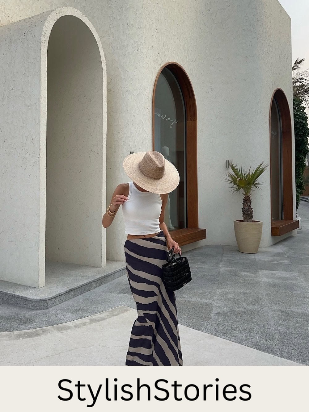 Woman wearing striped maxi skirt with a white tank and a straw hat.