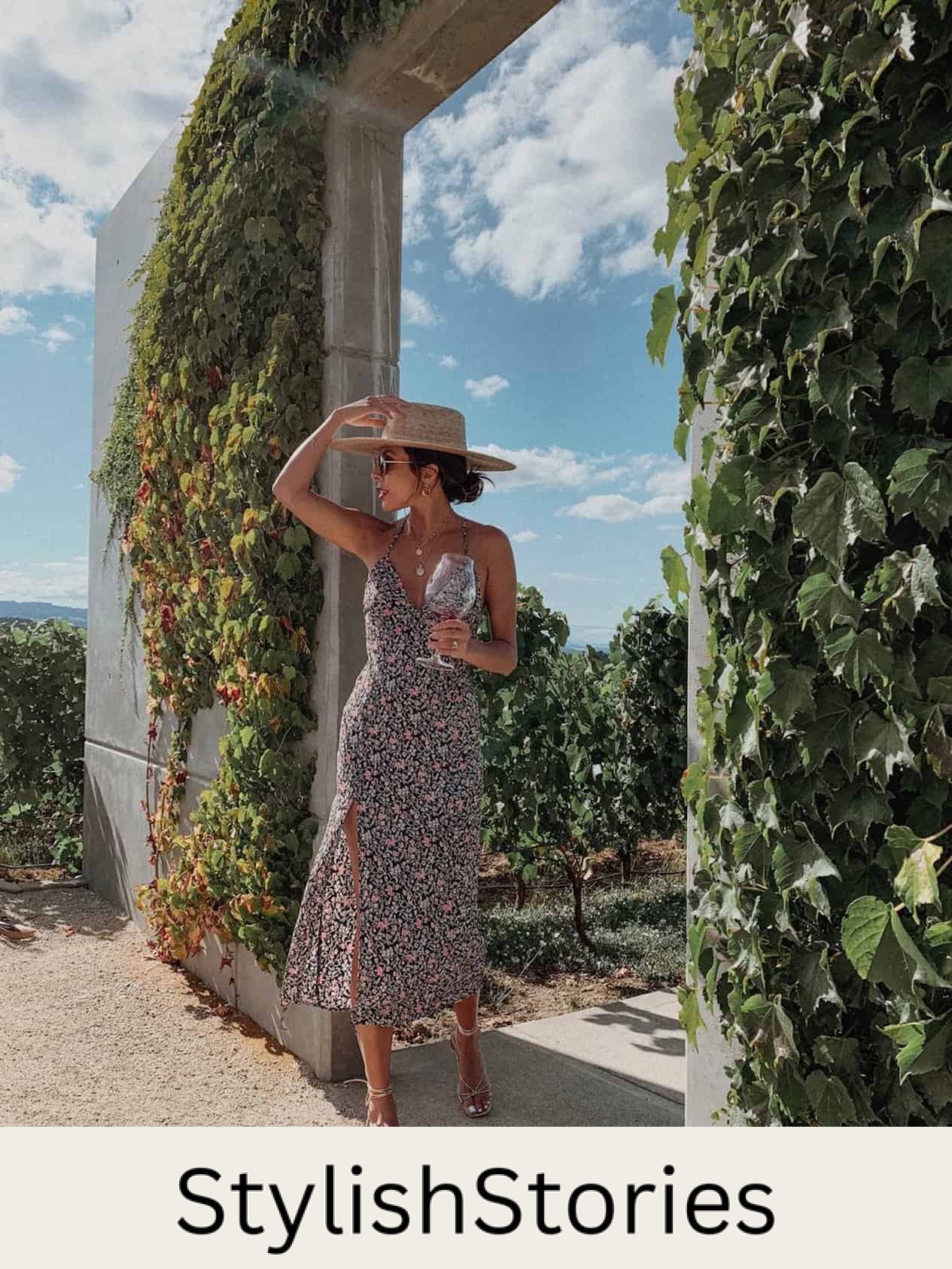 image of a woman in a floral midi dress with a sun hat holding a glass of wine at a winery