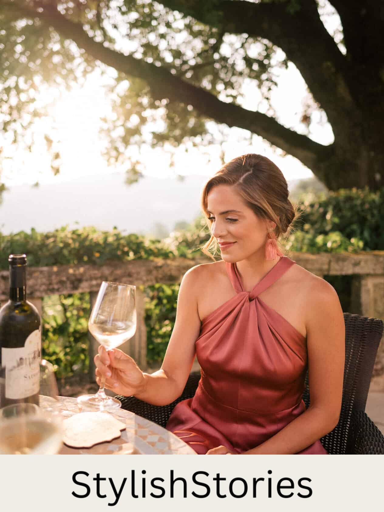 image of a woman in a dark blush satin dress sitting at a table drinking a glass of wine