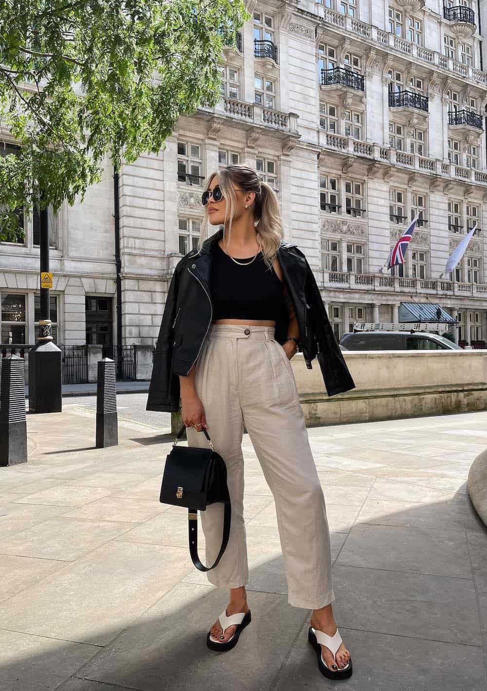 Woman wearing tan trousers, a black tank top and a black leather jacket.