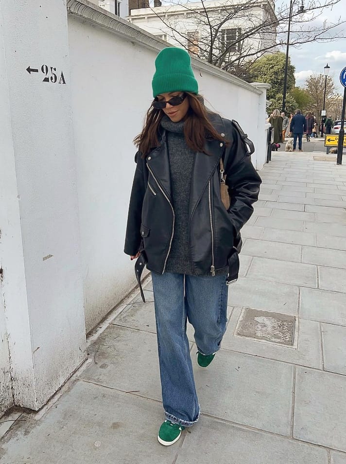 Woman wearing baggy jeans with an oversized sweater and leather jacket.