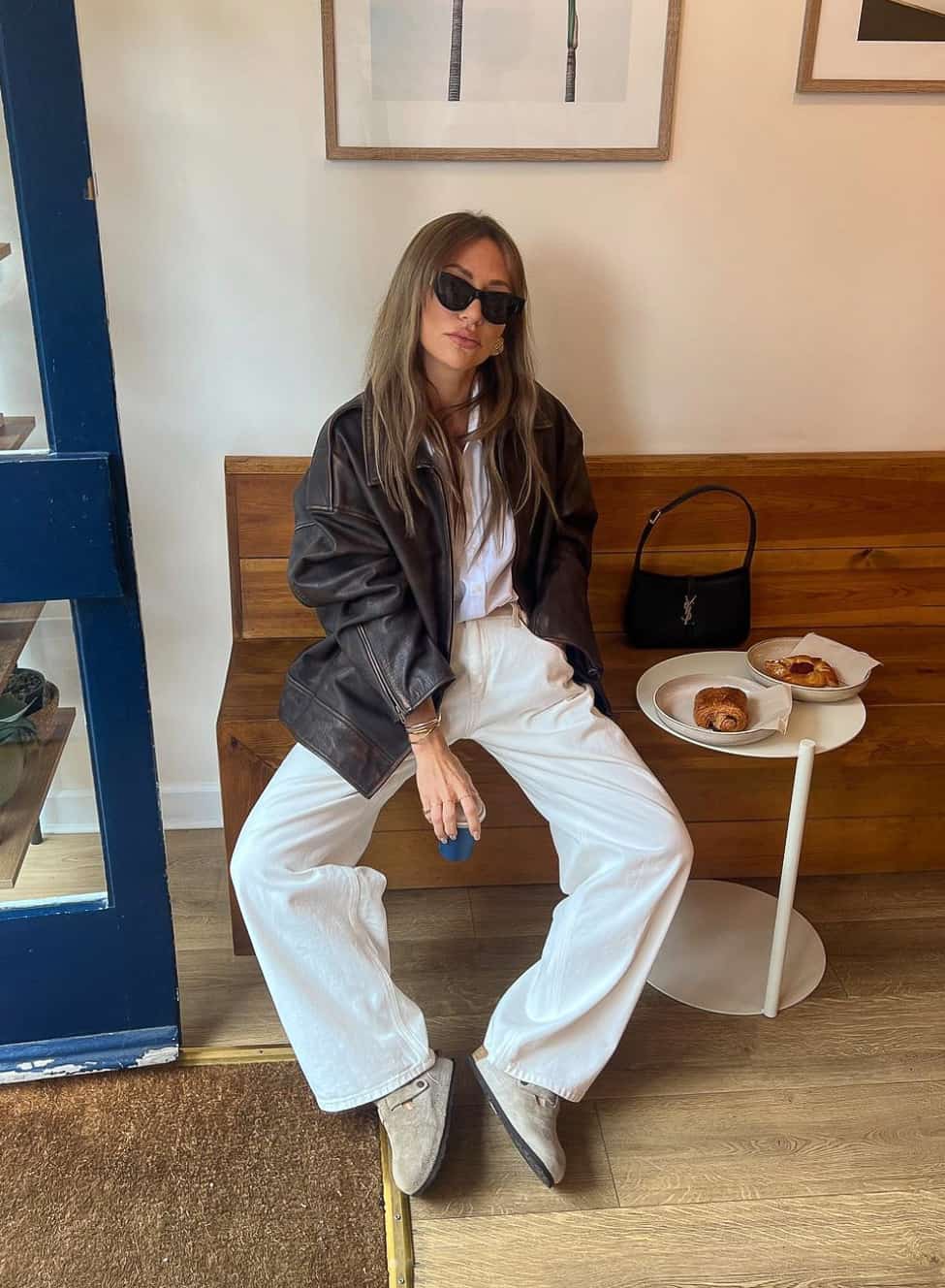 Woman wearing white jeans, a white button down and an oversized leather jacket.