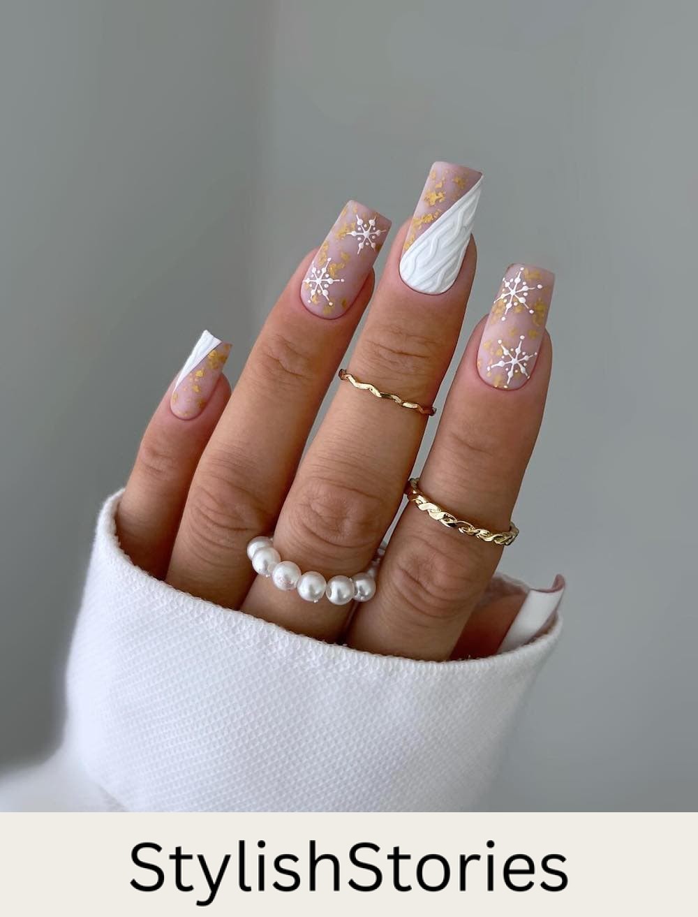 long square nails featuring beige base polish with white accents, snowflakes, and gold details