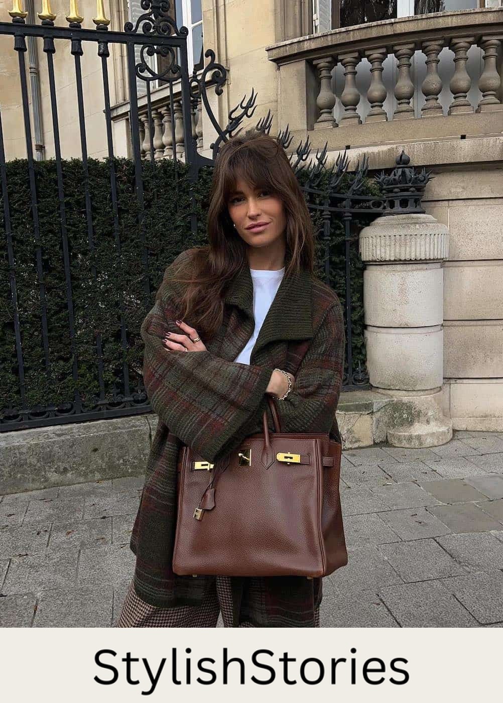 Woman wearing patterned pants and a plaid coat with a large brown handbag.