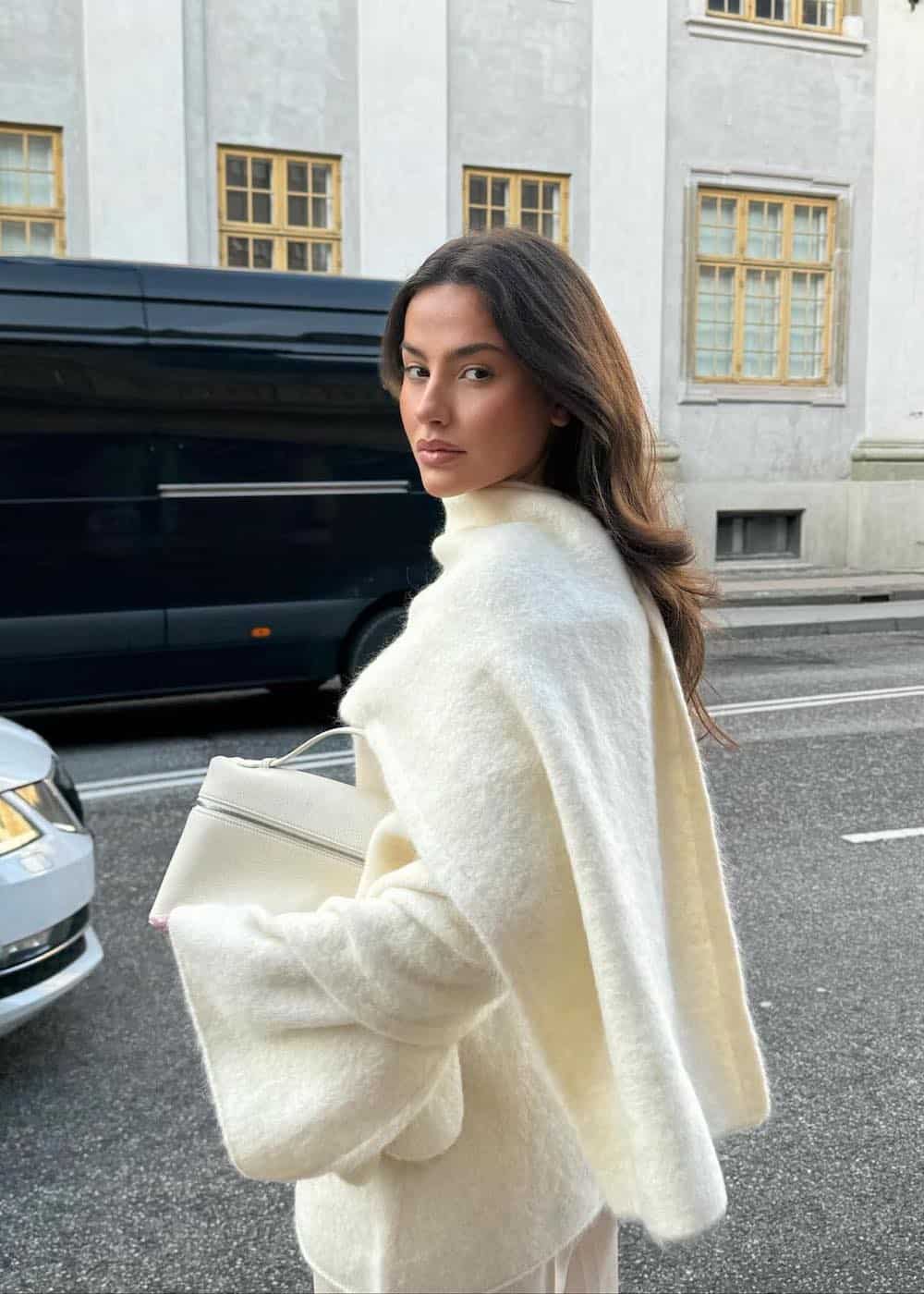 Woman wearing a large, white wrap scarf with a white sweater and white trousers.