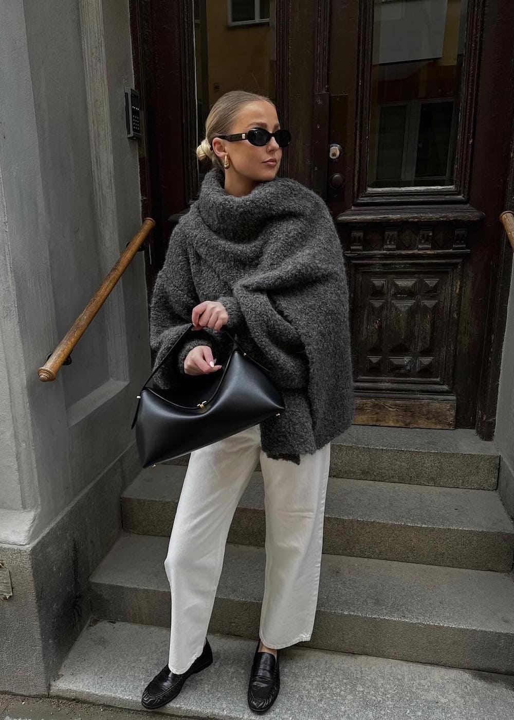 Woman wearing white jeans with black loafers and an oversized wrap scarf.